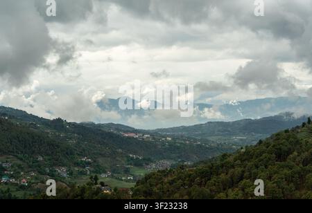 Eine Hochwinkelperspektive, die hinab in ein üppiges Bergtal in Mandi, Himachal Pradesh, Indien, blickt, wo eine ruhige Stadt zwischen dichten Wäldern liegt. Stockfoto