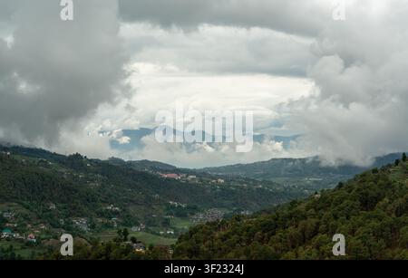 Ein weitläufiger Luftbildblick auf ein Bergtal in Mandi, Himachal Pradesh, Indien, mit einer kleinen Stadt, die sich in üppigen grünen Wäldern schmiegt Stockfoto