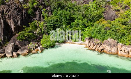 Ein abgelegener, unberührter Strand, geschützt von üppiger Vegetation und Granitfelsen, mit ruhigem türkisfarbenem Wasser. Stockfoto