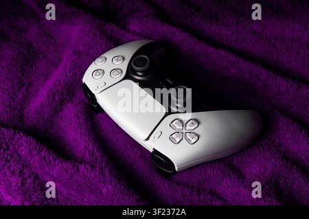 16. Juli 2026, Odessa, Ukraine. Weißer PlayStation 5 DualSense-Controller liegt auf einem strukturierten lila Stoffhintergrund. Stockfoto