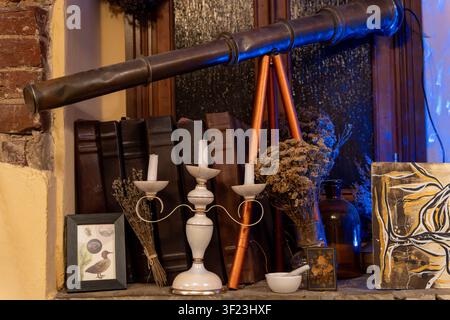 Auf einem Holzregal in einem alten Raum stehen ein Vintage-Teleskop, Kerzen und verschiedene Bücher. Getrocknete Blumen sind um die Gegenstände herum platziert. Die Atmosphäre Stockfoto