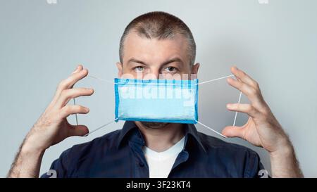 Mann Zeigt, Wie Man Medizinische Maske Im Studio, Panorama Tragen Stockfoto