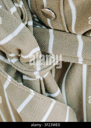 Detaillierte Nahaufnahme eines beigen gestreiften Leinenhemdes mit einem Knopf und natürlicher gewebter Stofftextur. Ideal für Mode, Bekleidung, Textilien, Schneiderei, Stockfoto