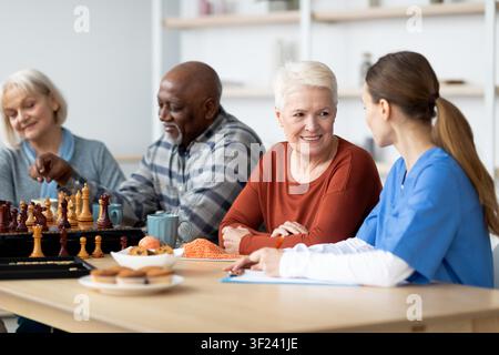 Lächelnde ältere kaukasische Frau und Mann spielen Schach in einem Gemeinschaftsaktivitätszentrum, Gesundheitskonzept Stockfoto