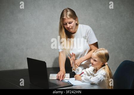 Mutter hilft ihrer Tochter beim Homeschooling, studiert in der Online-Schule mit Laptop zu Hause, Kind im Fernunterricht, Familienlebensstil modern Stockfoto