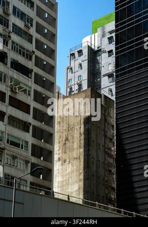 Bild von kontrastierenden Stadthochhäusern, das ein verwittertes Betongebäude zeigt, das zwischen modernen Handelstürmen unter blauem Himmel eingeklemmt ist Stockfoto