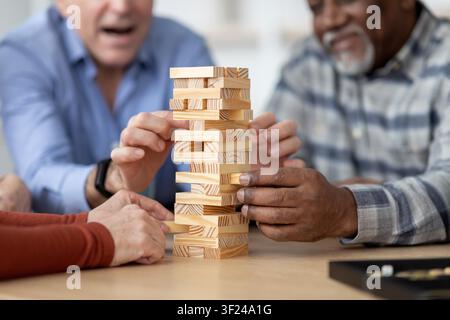 Glückliche ältere kaukasische Männer, die an einem Spiel teilnehmen, zu Hause gemeinsam Jenga spielen, nicht erkennbar Stockfoto