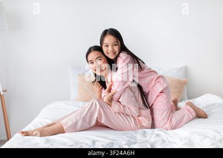 Lächelnde asiatische Mutter und Tochter spielen zusammen zu Hause, entspannen in Pyjamas Stockfoto