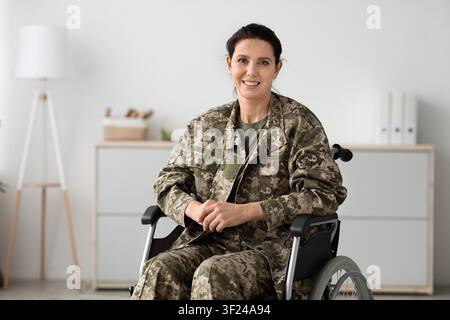 Lächelnde Soldatin im Rollstuhl in einem modernen Büro, Gesundheitskonzept Stockfoto