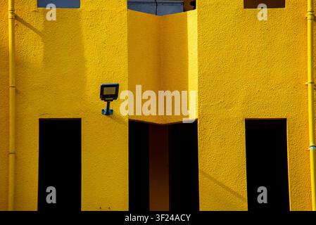 Dieses Bild zeigt ein modernes Gebäudeexterieur in einem auffälligen hellen Gelbton mit geometrischen Formen, Schatteneffekten und minimalistischer Architektur Stockfoto