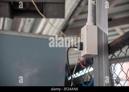 Nahaufnahme einer elektrischen Steckdose, die an einem Gebäudegerüst in einer Industrie- oder Baustelle montiert ist, mit sichtbarer Verkabelung, Leitungsrohren und strukturelem Element Stockfoto