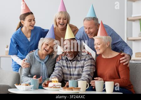 Fröhliche diverse Gruppe feiert Geburtstag mit Kuchen und Kerzen zu Hause, Familienkonzept Stockfoto