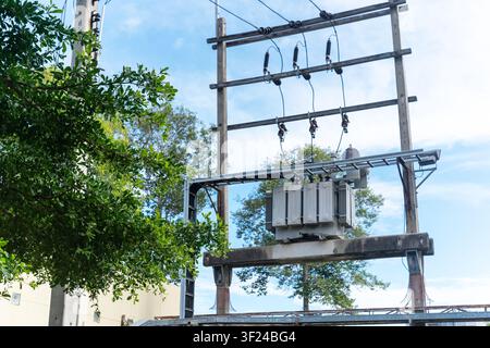 Dieses Bild zeigt eine Außenanlage mit einem hölzernen Versorgungsmast, der einen elektrischen Transformator und Freileitungen unterstützt, und zeigt elektrische Stockfoto