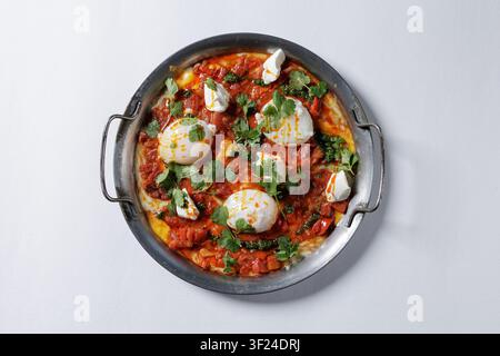 Ein farbenfrohes Shakshuka-Gericht mit pochierten Eiern, würziger Tomatensoße und frischen Kräutern, perfekt für Frühstücks- oder Brunch-Menüs in Restaurants und Lebensmittelläden Stockfoto