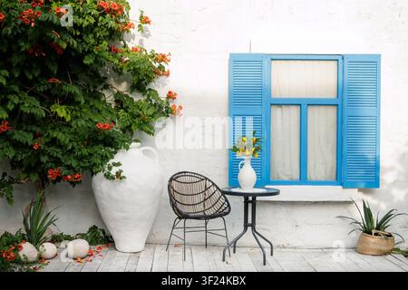 Eine ruhige Außenterrassen-Szene mit blauen Fensterläden, einem stilvollen Stuhl und lebendigen Pflanzen, perfekt für Inspirationen zur Inneneinrichtung oder Lifestyle-Inhalte. Stockfoto