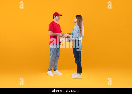 Lächelnder junger kaukasischer Mann liefert Paket an Frau, gelber Hintergrund, Lieferkonzept Stockfoto
