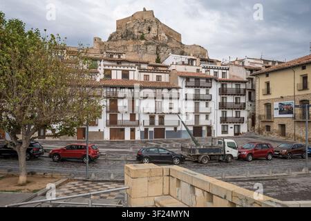 Traditionelle weiße Gebäude mit Holzbalustern auf einem Stadtplatz in Morella, Spanien, mit einer mittelalterlichen Burg auf einem felsigen Hügel im Hintergrund. Stockfoto