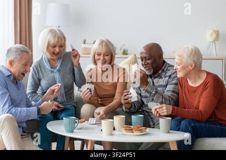 Glückliche Seniorengruppe spielt zusammen zu Hause Karten, lächelt und genießt das Leben Stockfoto