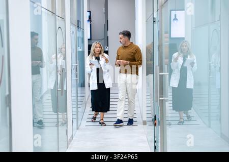 Ärzte gehen und besprechen Patienteninformationen in einem hellen Krankenhausflur Stockfoto