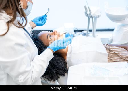Zahnarzt in Schutzhandschuhen und Maske untersucht die Mundgesundheit eines Patienten in einer Klinik Stockfoto