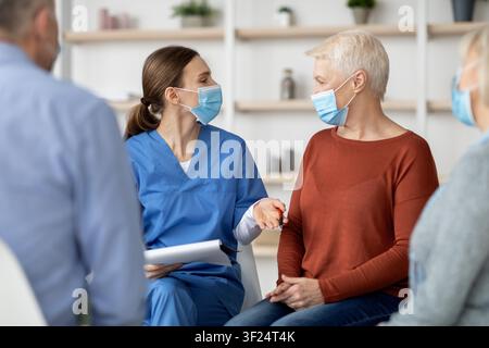 Konzentrierte kaukasische Gesundheitsfachkraft spricht mit einer älteren Frau in der Klinik, Gesundheitskonzept Stockfoto