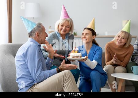 Zufriedener älterer kaukasischer Mann feiert Geburtstag mit Familie und Kuchen in einer häuslichen Umgebung Stockfoto
