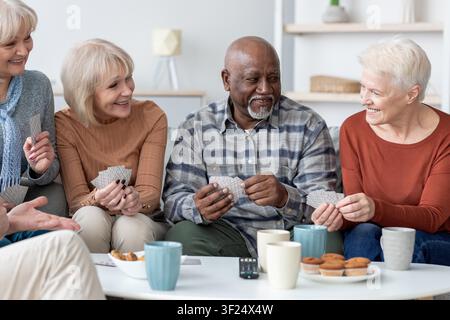 Glückliche Senioren spielen zusammen Karten und lächeln in einem hellen modernen Wohnzimmer Stockfoto