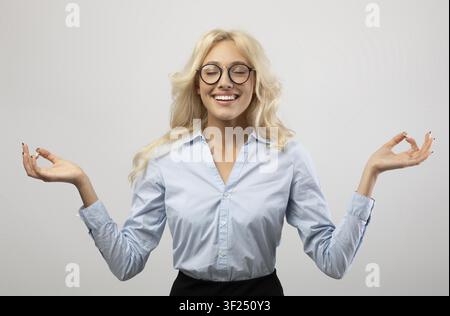 Lächelnde junge kaukasische Frau, die im Büro Meditation praktiziert, Wellness-Konzept Stockfoto