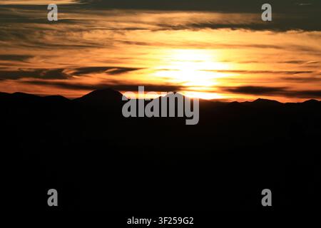 Intensiver orange-blauer Sonnenuntergangshimmel mit dramatischen Wolkenformationen über entfernten Bergkämmen. Stockfoto