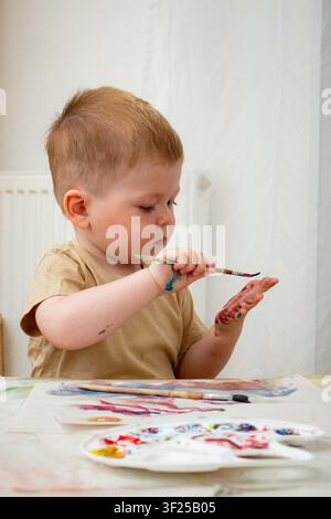 Kind mischt Wasserfarben mit den Fingern auf Papier. Taktiles Lernen über Farbmischung. Sensorisches Spiel stärkt neuronale Verbindungen. Kunsttherapie und ar Stockfoto