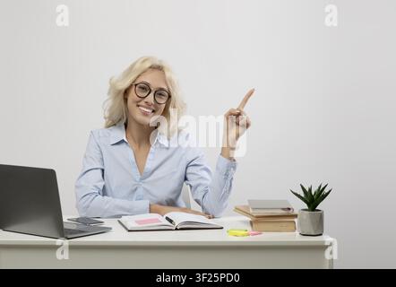 Lächelnde junge kaukasische Frau, die im Büro auf ein Notizbuch zeigt, Geschäftskonzept Stockfoto