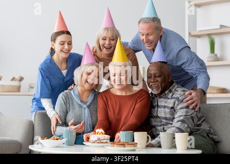 Fröhliche Gruppe von Senioren feiert gemeinsam den Geburtstag in einem gemütlichen Wohnzimmer, freudiger Moment Stockfoto