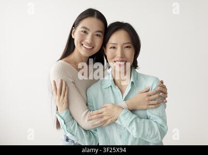 Glückliche junge asiatische Frau und Mutter umarmen sich, lächeln, Studioeinstellung Stockfoto
