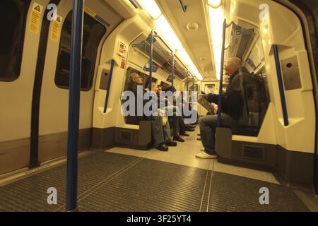 Passagiere sitzen in einem U-Bahn-Waggon, beleuchtet von Deckenleuchten, die London Underground. UK Stockfoto