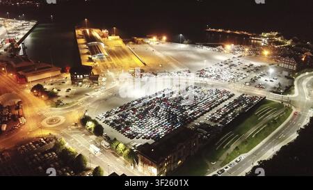 Nachtansicht eines großen Parkplatzes voller importierter Autos, hell beleuchtet in der Nähe eines Ufergebiets, Drohnenfotografie, Southampton, UK Stockfoto