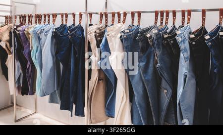 Kleiderständer hält mehrere Denimjeans. Hellblaue, dunkelblaue und beigefarbene Nuancen sind sichtbar. Jeans hängen ordentlich auf Bügeln in einem Einzelhandelsraum. Organisiert Stockfoto