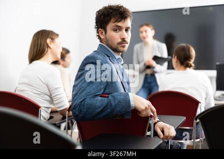 Positiver junger Mann, der sich umdreht und in die Kamera schaut während des Fortbildungskurses im Gehör Stockfoto