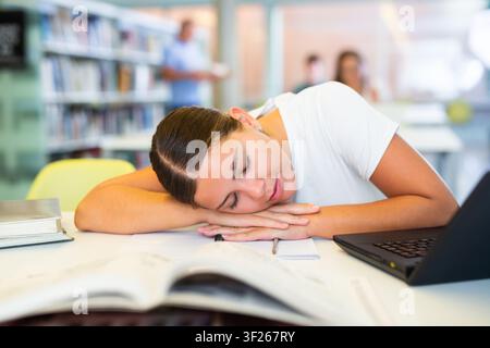Müde Studentin schlief am Tisch in der Bibliothek ein Stockfoto