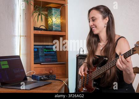 Junge Frau nimmt Bassgitarre in einem Heim-Musikstudio auf Stockfoto