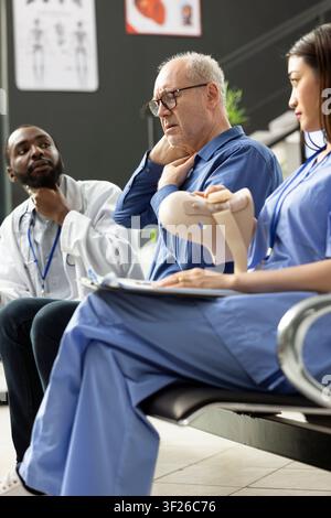 Seniorer Mann mit Nackenschmerzen und Muskelbeschwerden, der müde und gestresst in der Kliniklobby erscheint. Die Szene spiegelt gesundheitliche Herausforderungen und professionelle Beratung in einem modernen Krankenhaus wider. Stockfoto