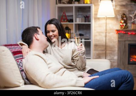 Entspanntes Paar sitzt zusammen auf einer Couch und feiert den Weihnachtstag, zeigt einen ruhigen Feiertagsmoment in einem komfortablen Wohnraum-Interieur. Stockfoto