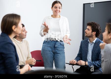 Junge Lehrerin, die Antworten von Schülern unterschiedlichen Alters hört, während sie im Kreis beim Fremdsprachenunterricht sitzt Stockfoto
