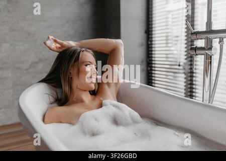 Lächelnde junge Frau genießt ein Schaumbad zu Hause, Entspannungskonzept Stockfoto
