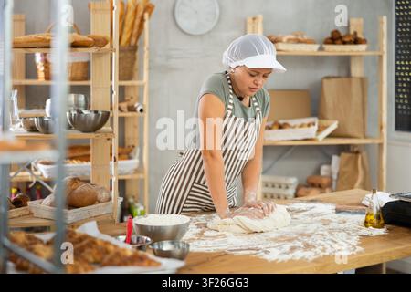 Frau arbeitet in der Bäckerei als Bäckerin, knetet Teig, arbeitet mit Mehl. Stockfoto