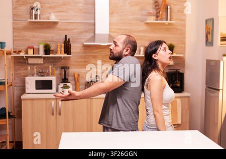 Ehemann und Ehefrau sitzen Rücken an Rücken nach einem Vorwurf der Untreue und zeigen Frustration, Uneinigkeit und Beziehungsstress zu Hause. Stockfoto