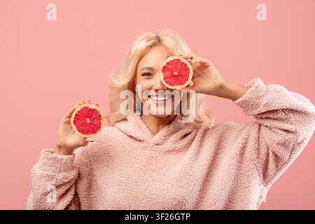 Glückliche junge Frau hält Grapefruitscheiben, lächelt in einem kuscheligen Pullover, Studio, Wellness-Konzept Stockfoto