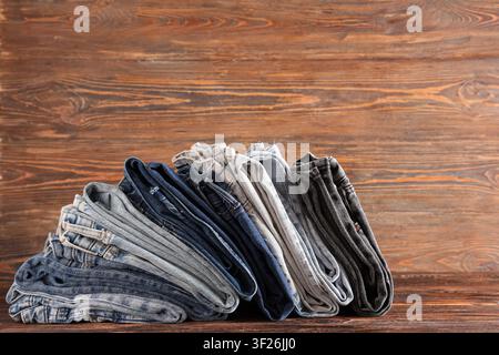 Stapel gefalteter Denimjeans in verschiedenen Blautönen und Grautönen auf einem rustikalen Holzgrund, die Kleidungsstücke sind ordentlich organisiert, verschiedene Waschungen Stockfoto
