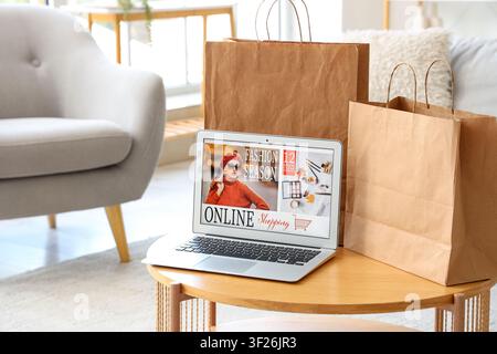 Laptop zeigt Online-Modeeinkaufsseite mit braunen Papiertüten auf einem Holztisch in einem hellen Wohnzimmer, Set, Computer Stockfoto