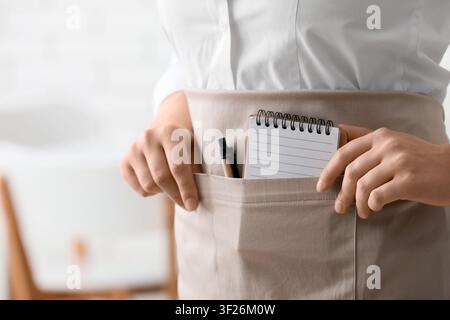 Kellnerin oder Barista trägt eine beige Schürze mit einem Notizblock und einem Stift in der Tasche, bereit, Bestellungen entgegenzunehmen Stockfoto