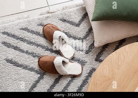 Paar gemütliche braune Wildlederpantoffeln mit weißem Kunstfellfutter auf einem gemusterten Teppich, Komfort und Entspannung zu Hause, die weiche Textur der Pantoffeln und Stockfoto